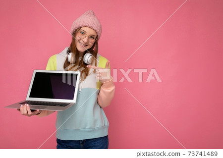 Photo of smiling happy charming Pretty young woman wearing hat colorful sweater and glasses holding 73741489