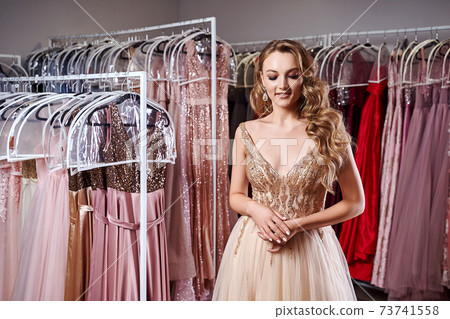 Beautiful blonde girl wearing a full-length yellow champaign chiffon slit prom ball gown decorated with golden sequins. Model in dress hire service with many dresses in different color and style. Beautiful blonde girl wearing a full-length yellow champaign chiffon slit prom ball gown decorated with golden sequins. Model in dress hire service with many dresses in different color and style. 73741558