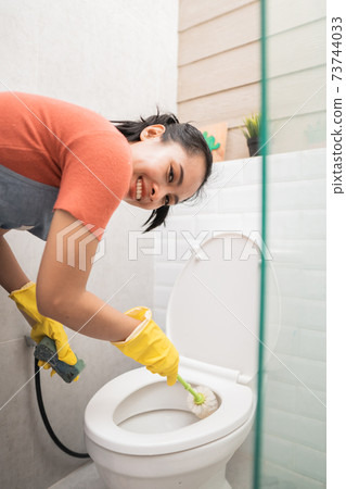 Asian women wearing gloves clean the toilet with a brush and porcelain cleaner 73744033