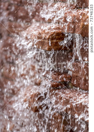 Close up view of glistening water running down a red brick stone wall Close up view of glistening water running down a red brick stone wall 73746183