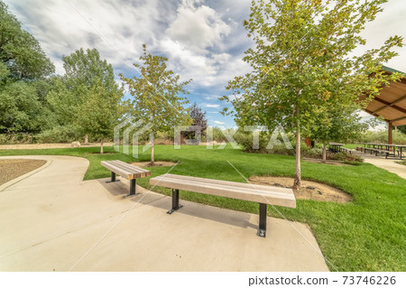 Park with wooden benches along pathway and picnic pavilion in the background 73746226