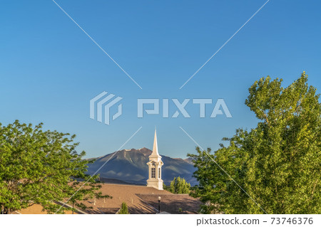 White spire and brown roof of church with mountain and clear blue sky background White spire and brown roof of church with mountain and clear blue sky background 73746376