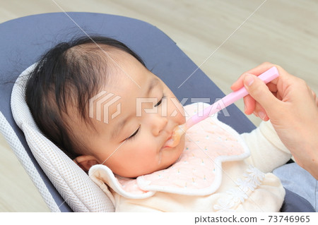 Baby feeding baby food in the living room 73746965
