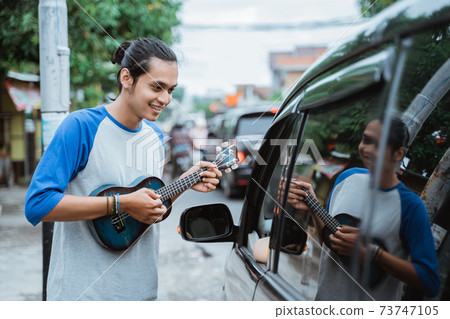 busker use musical instruments and sing beside a car 73747105
