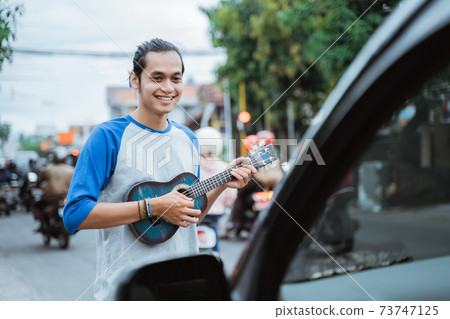 busker use musical instruments and sing in front of the car on the traffic lights crossroad 73747125