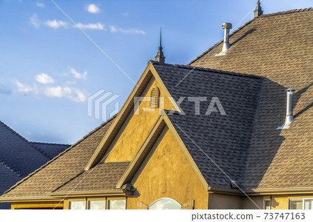 Close up of the roof and brown wall of a home against blue sky on a sunny day 73747163