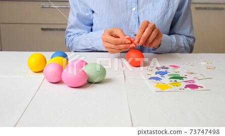 female hands paints eggs in pastel colors for Easter and decorates with birds in the decor, sitting female hands paints eggs in pastel colors for Easter and decorates with birds in the decor, sitting 73747498