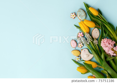 Sweets for celebrate Easter. Gingerbread in shape of easter bunny, flowers and easter eggs, seasonal flowers tulips. Blue background, top view, copy space, banner for your site, flyer, invitation 73751186