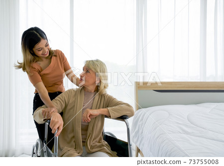 Happy mix skin family living together, asian daughter takes care of her adopted caucasian mother sitting on a wheelchair. Concept of love and sharing time of family, mother or daughter in law. Happy mix skin family living together, asian daughter takes care of her adopted caucasian mother sitting on a wheelchair. Concept of love and sharing time of family, mother or daughter in law. 73755008