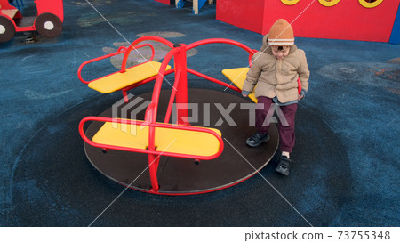 Little boy in warm hat and jacket rides on merry-go-round Little boy in warm hat and jacket rides on merry-go-round 73755348