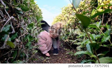Funny girl in stylish jacket plays between bushes in park Funny girl in stylish jacket plays between bushes in park 73757001