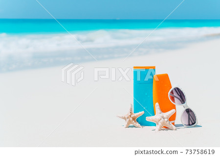 Suncream bottles, sunglasses, starfish on white sandy beach 73758619