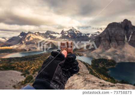 Hiker man with glove holding chocolate piece on peak of mountain 73758873