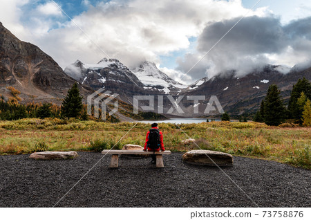 Traveler man sitting on beach with mount assiniboine and lake magog in provincial park 73758876