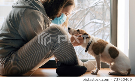 Woman sitting in mask at window with a dog 73760409