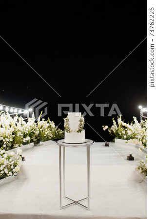 wedding white cake on a high stand near the white podium 73762226