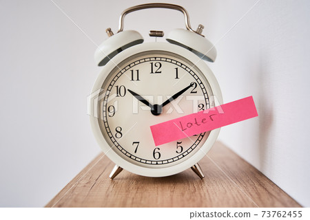 Procrastination and delay concept. Sticky note with word later on white alarm clock. Urgency time Procrastination and delay concept. Sticky note with word later on white alarm clock. Urgency time 73762455