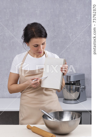 Woman chef is holding cookbook in the kitchen holding cooking class. Vertical frame Woman chef is holding cookbook in the kitchen holding cooking class. Vertical frame 73762870