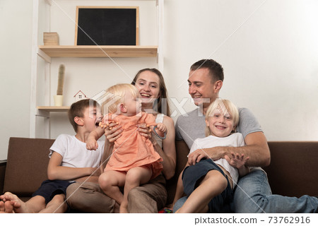 Mom dad and three children are sitting together on couch. Big friendly family Mom dad and three children are sitting together on couch. Big friendly family 73762916