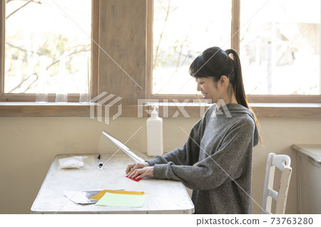 A woman doing origami at a table by the window 73763280
