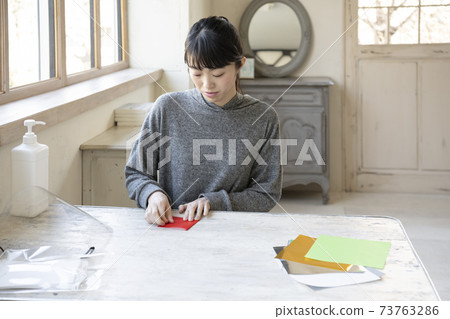 A woman doing origami at a table by the window 73763286