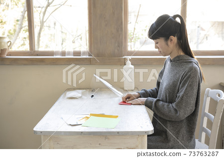 A woman doing origami at a table by the window 73763287