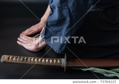 A person sitting upright and a Japanese sword 73764225