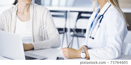Unknown woman-doctor sitting and communicating with female patient. Physician checks medical history record and exam results, close-up. Healthcare concept 73764805