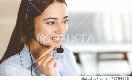 Brunette female customer service representative using headset and consulting clients online. Call center Brunette female customer service representative using headset and consulting clients online. Call center 73764806