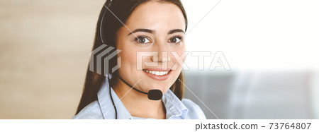 Brunette female customer service representative using headset and consulting clients online. Call center Brunette female customer service representative using headset and consulting clients online. Call center 73764807