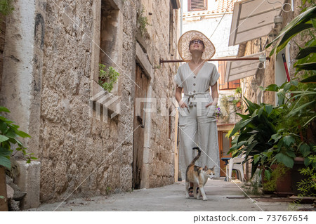 Beautiful blonde young female traveler wearing straw sun hat sightseeing and enjoying summer vacation in an old traditional costal town at Adriatic cost, Croatia. Beautiful blonde young female traveler wearing straw sun hat sightseeing and enjoying summer vacation in an old traditional costal town at Adriatic cost, Croatia. 73767654