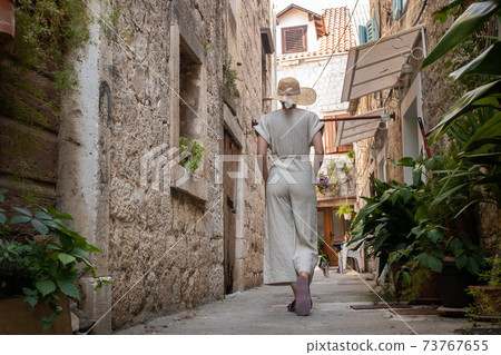 Rear view of beautiful blonde young female traveler wearing straw sun hat sightseeing and enjoying summer vacation in an old traditional costal town at Adriatic cost, Croatia 73767655