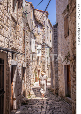 Rear view of beautiful blonde young female traveler wearing straw sun hat sightseeing and enjoying summer vacation in an old traditional costal town at Adriatic cost, Croatia Rear view of beautiful blonde young female traveler wearing straw sun hat sightseeing and enjoying summer vacation in an old traditional costal town at Adriatic cost, Croatia 73767656