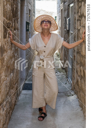Beautiful blonde young female traveler wearing straw sun hat sightseeing and enjoying summer vacation in an old traditional costal town at Adriatic cost, Croatia. Beautiful blonde young female traveler wearing straw sun hat sightseeing and enjoying summer vacation in an old traditional costal town at Adriatic cost, Croatia. 73767658