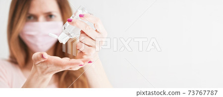 Young woman with home made pink cotton face mouth virus mask dropping anti bacterial alcohol rubbing gel on hand, blurred face back, wide photo, empty space right side Coronavirus covid-19 prevention Young woman with home made pink cotton face mouth virus mask dropping anti bacterial alcohol rubbing gel on hand, blurred face back, wide photo, empty space right side Coronavirus covid-19 prevention 73767787