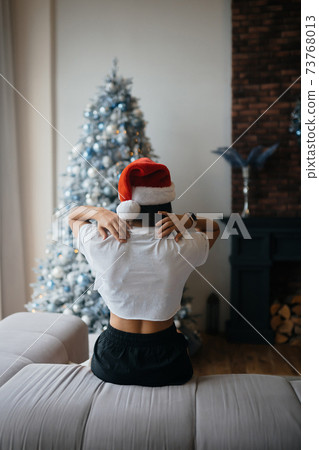 Smiling woman with santa hat on head in living room Smiling woman with santa hat on head in living room 73768013