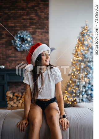 Smiling woman with santa hat on head in living room Smiling woman with santa hat on head in living room 73768018