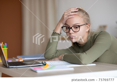 Bored teen girl sitting at home with book, doing homework Bored teen girl sitting at home with book, doing homework 73769777