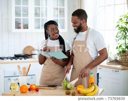 Happy Black Couple Checking Recipe In Cookbook While Cooking Together In Kitchen Happy Black Couple Checking Recipe In Cookbook While Cooking Together In Kitchen 73769830