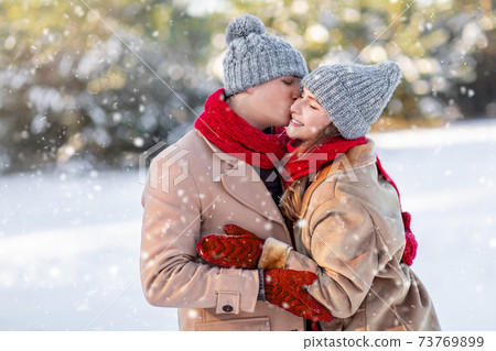 Loving man kissing his happy girlfriend over winter forest 73769899
