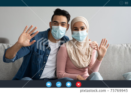 Muslim couple in face masks waving at camera, laptop screen 73769945