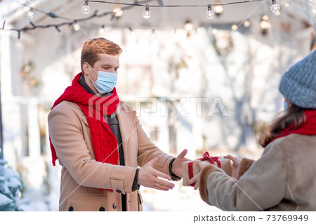 Guy in face mask getting present from woman, standing outdoors 73769949