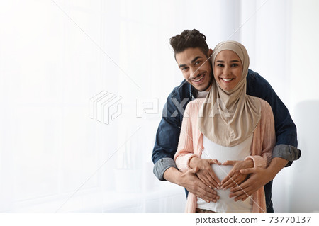 Portrait of happy pregnant religious muslim couple posing near window at home 73770137