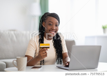 Smiling african woman holding credit card, using laptop Smiling african woman holding credit card, using laptop 73770513
