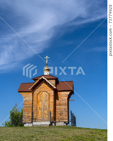 Small old wooden chapel on summer green grassy hill top, and blue sky with cloud. 73774928