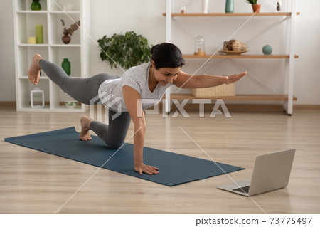 Active indian female practice static tiger asana look at laptop 73775497