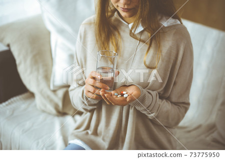 Close-up woman holding pills time to take medications, cure for headache, high blood pressure or cholesterol level remedy pain killer drugs. Stay at home concept during Coronavirus pandemic and self Close-up woman holding pills time to take medications, cure for headache, high blood pressure or cholesterol level remedy pain killer drugs. Stay at home concept during Coronavirus pandemic and self 73775950