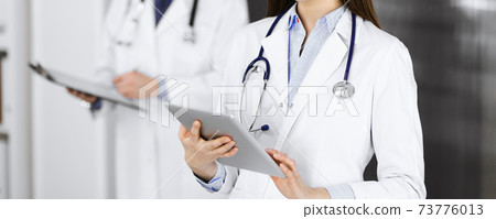 Unknown woman doctor iusing tablet computer in her hands, while standing in clinic. Medicine concept during Coronavirus pandemic 73776013
