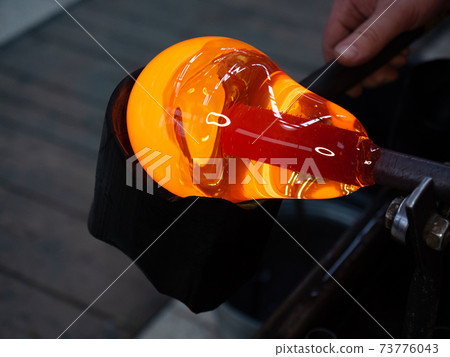 Shaping the red melted glass on  glassblowing pipe 73776043