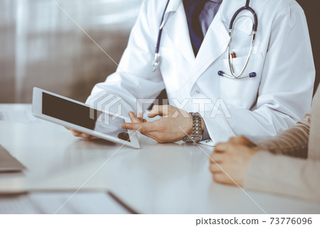 Unknown male doctor and patient woman discussing something while sitting in clinic and using tablet computer. Best medical service in hospital, medicine, pandemic stop Unknown male doctor and patient woman discussing something while sitting in clinic and using tablet computer. Best medical service in hospital, medicine, pandemic stop 73776096
